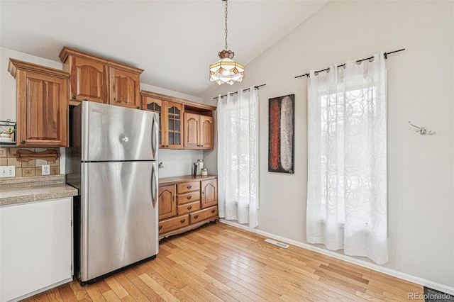 280 Pierce St, Erie, CO 80516 - kitchen featuring freestanding refrigerator, lofted ceiling, brown cabinets, light wood-style flooring, and glass insert cabinets
