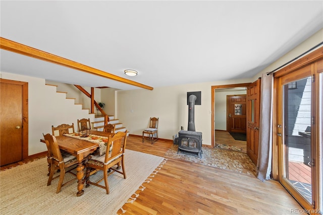 dining space featuring a wood stove, light wood-type flooring, stairs, and baseboards