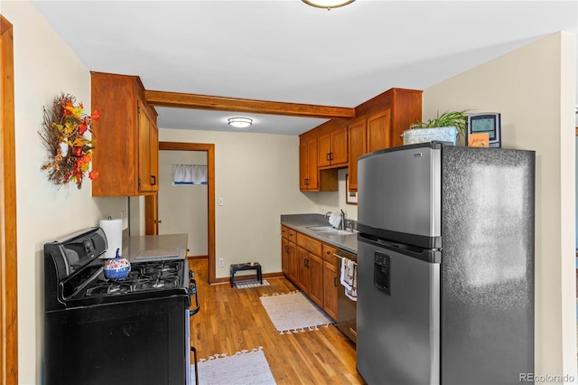 kitchen featuring stainless steel appliances, light wood-style flooring, a sink, dark countertops, and brown cabinetry