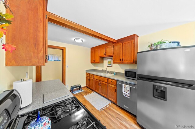 kitchen featuring stainless steel appliances, a sink, light wood-style flooring, brown cabinetry, and beam ceiling
