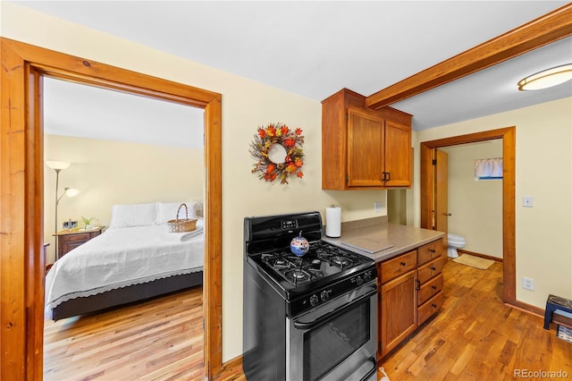 kitchen with stainless steel range with gas stovetop, light wood-style floors, beamed ceiling, baseboards, and brown cabinetry