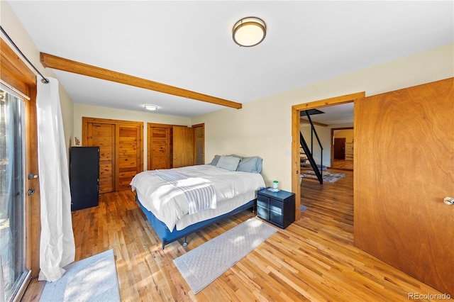bedroom featuring light wood-style floors, multiple closets, and beamed ceiling