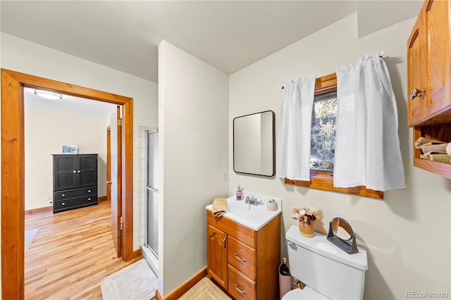 bathroom with vanity, wood finished floors, a stall shower, toilet, and baseboards