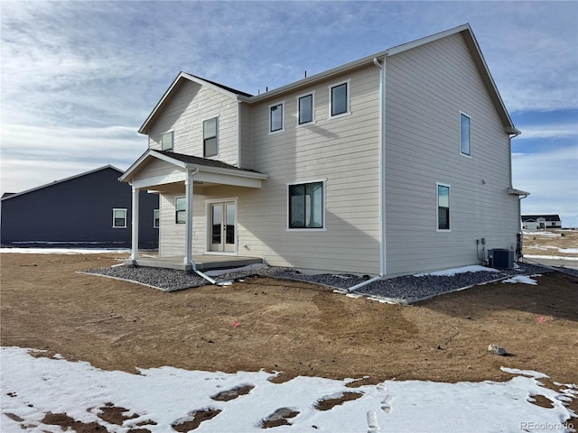 snow covered back of property with cooling unit and a patio area