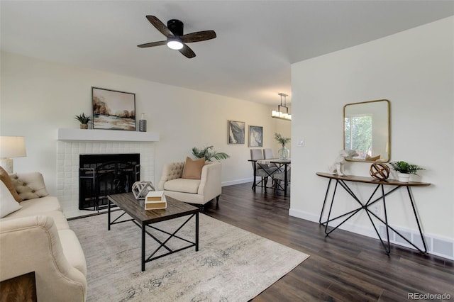 living room with a brick fireplace, dark hardwood / wood-style floors, and ceiling fan