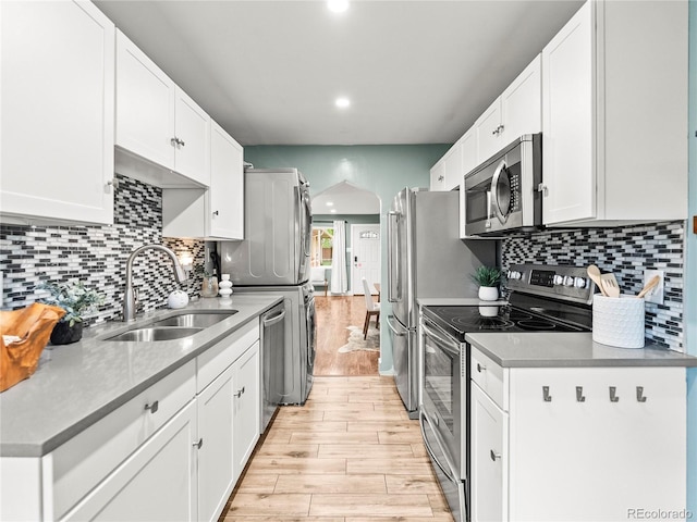 3555 Leyden St, Denver, CO 80207 - kitchen featuring appliances with stainless steel finishes, a sink, stacked washer / drying machine, light wood-type flooring, and arched walkways