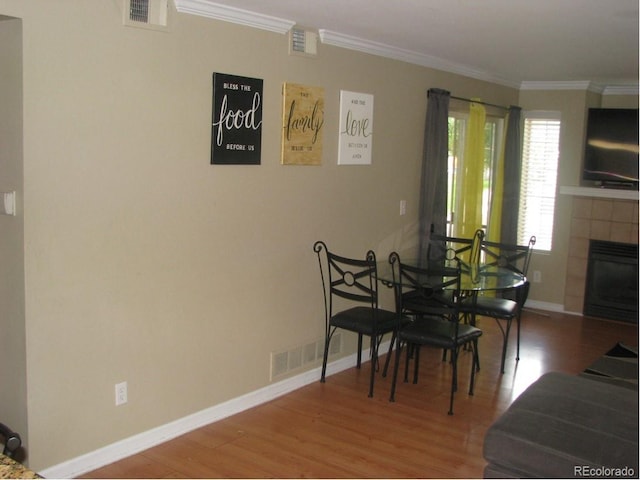 dining area featuring a tile fireplace, hardwood / wood-style floors, and ornamental molding