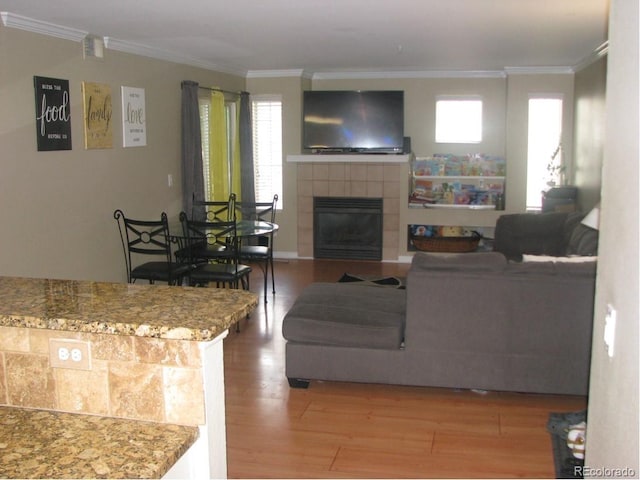 living room with hardwood / wood-style floors, ornamental molding, and a tiled fireplace