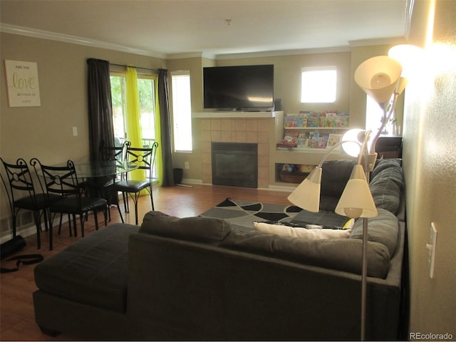 living room featuring hardwood / wood-style floors, crown molding, a healthy amount of sunlight, and a tiled fireplace