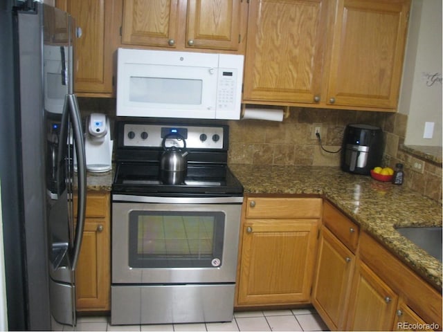 kitchen featuring light tile patterned flooring, stainless steel appliances, tasteful backsplash, and dark stone countertops