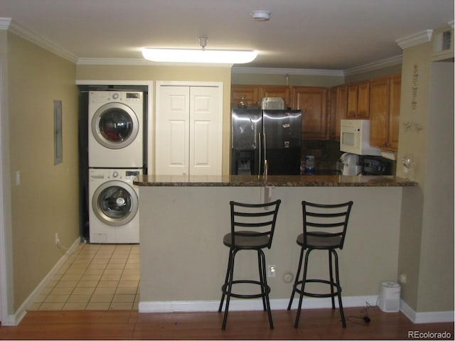 kitchen featuring refrigerator, crown molding, light tile patterned floors, stacked washer / drying machine, and a kitchen bar