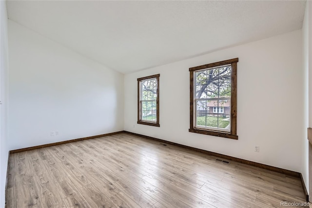 empty room with light wood finished floors, lofted ceiling, and baseboards