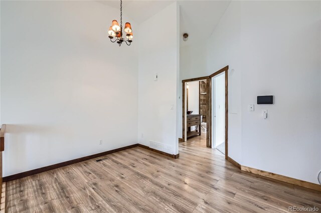 empty room with a chandelier, light wood-style flooring, baseboards, and a towering ceiling