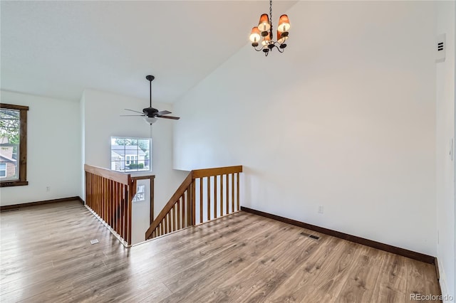 empty room featuring plenty of natural light, a chandelier, wood finished floors, a ceiling fan, and high vaulted ceiling