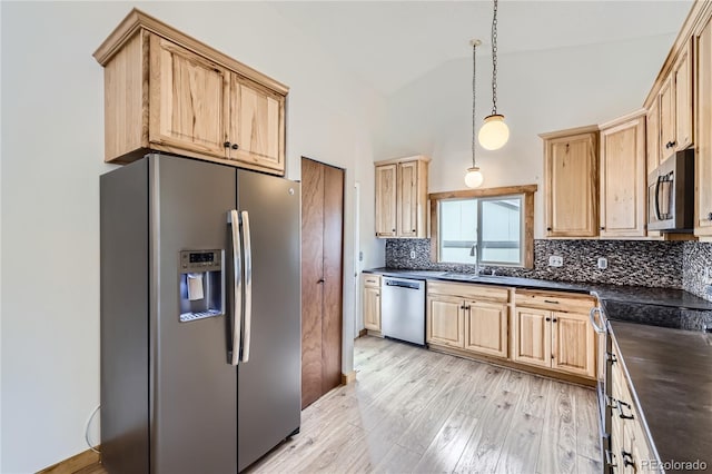 kitchen featuring appliances with stainless steel finishes, a sink, light brown cabinets, vaulted ceiling, and backsplash