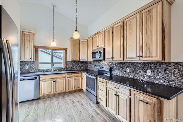 kitchen with stainless steel appliances, a sink, light brown cabinets, dark countertops, and high vaulted ceiling