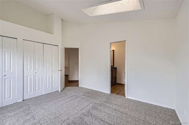 unfurnished bedroom featuring carpet flooring, lofted ceiling, baseboards, multiple closets, and ensuite bathroom