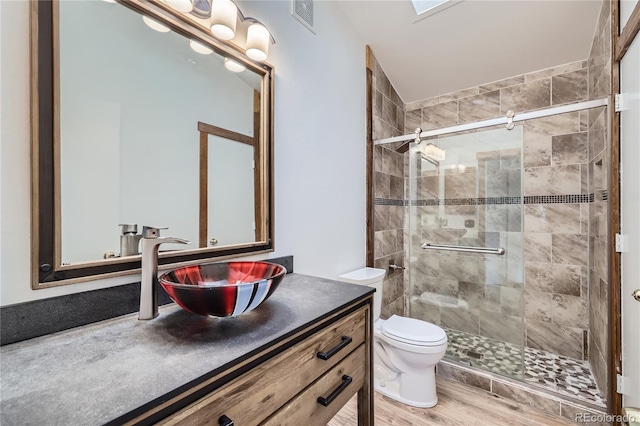 bathroom with a stall shower, toilet, vanity, and wood finished floors