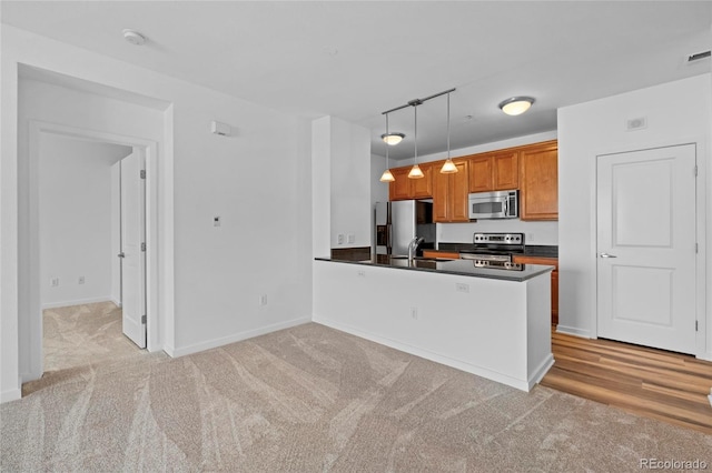 4100 Albion St Unit 320, Denver, CO 80216 - kitchen featuring stainless steel appliances, dark countertops, light carpet, a peninsula, and hanging light fixtures