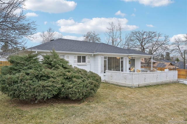 rear view of house with a lawn, fence, and roof with shingles