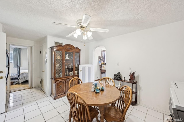 dining area featuring light tile patterned floors, arched walkways, a textured ceiling, and a ceiling fan