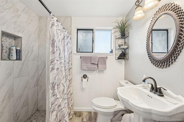 full bathroom with wood finished floors, baseboards, tiled shower, a sink, and toilet