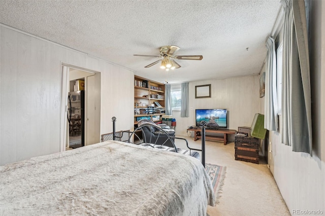 bedroom featuring freestanding refrigerator, ceiling fan, wood walls, a textured ceiling, and light carpet