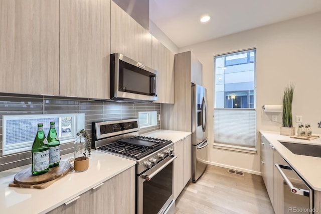 3256 Federal Blvd, Denver, CO 80211 - kitchen featuring appliances with stainless steel finishes, modern cabinets, light countertops, tasteful backsplash, and light wood finished floors