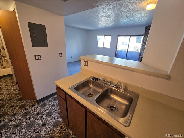 kitchen with a textured ceiling, light countertops, a sink, and electric panel