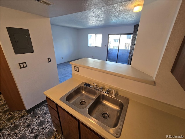 kitchen with light countertops, electric panel, a sink, and a textured ceiling