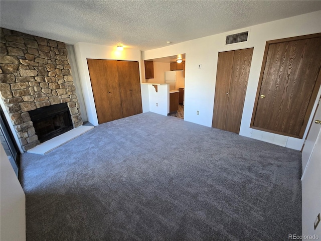 unfurnished living room with carpet floors, visible vents, a fireplace, and a textured ceiling