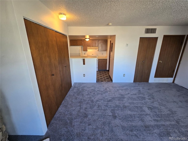 unfurnished bedroom featuring a textured ceiling, carpet floors, visible vents, multiple closets, and freestanding refrigerator