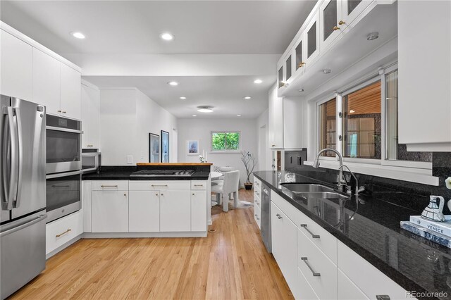 kitchen featuring light wood finished floors, a peninsula, a sink, white cabinetry, and appliances with stainless steel finishes