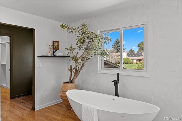 full bath with a soaking tub, baseboards, and wood finished floors