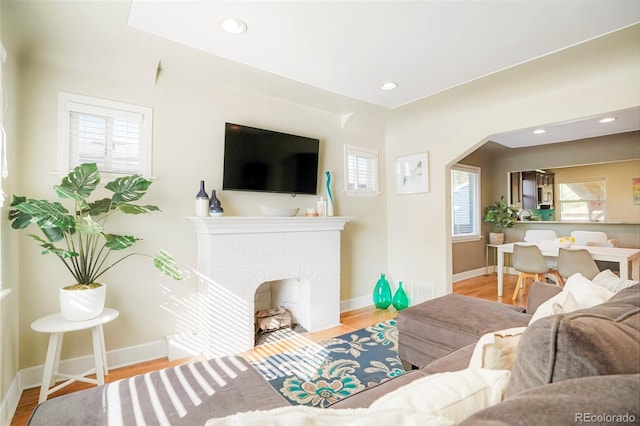 living room featuring a brick fireplace, light hardwood / wood-style flooring, and a wealth of natural light