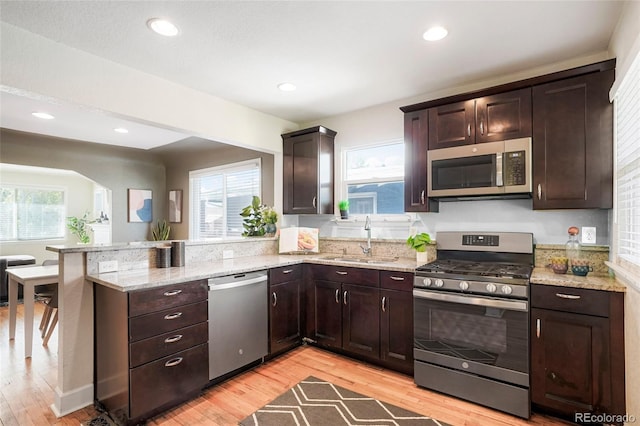 kitchen with appliances with stainless steel finishes, sink, dark brown cabinets, and light wood-type flooring