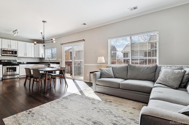 living room featuring dark hardwood / wood-style flooring, sink, crown molding, and an inviting chandelier