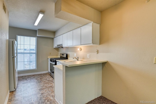 kitchen featuring stainless steel gas range oven, white cabinets, a textured ceiling, white fridge, and kitchen peninsula