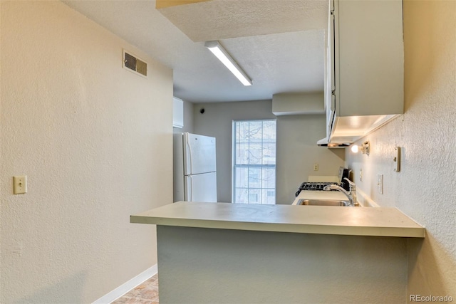 kitchen featuring kitchen peninsula, stainless steel range with gas cooktop, sink, and white refrigerator