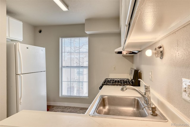 kitchen with stainless steel range, white refrigerator, white cabinets, and sink