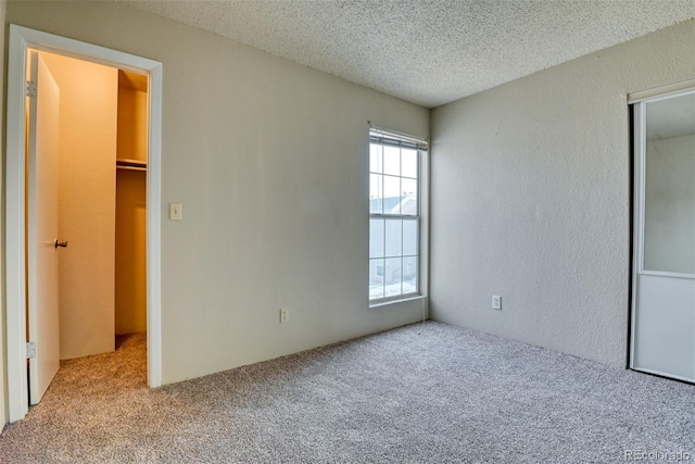 unfurnished bedroom with multiple windows, a spacious closet, light colored carpet, and a textured ceiling