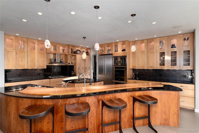 kitchen featuring glass insert cabinets, built in appliances, a large island with sink, and dark countertops