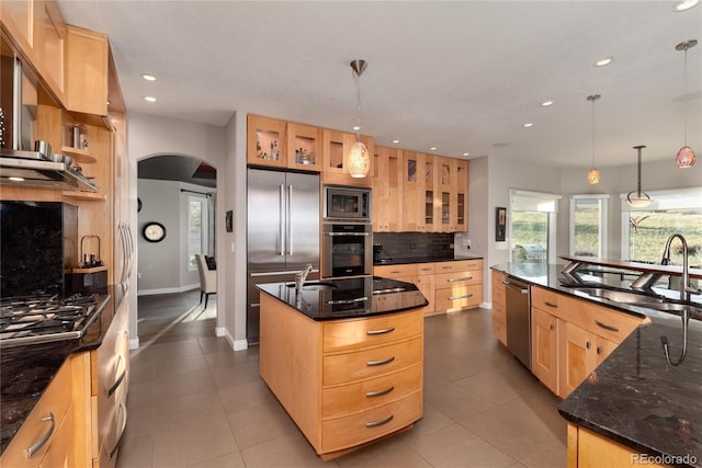 kitchen featuring arched walkways, light brown cabinetry, a large island, a sink, and built in appliances