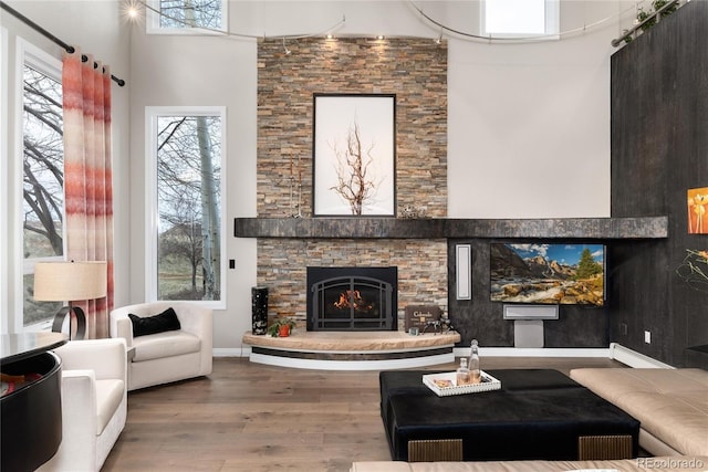 living room featuring a fireplace, wood finished floors, a high ceiling, a baseboard radiator, and baseboards