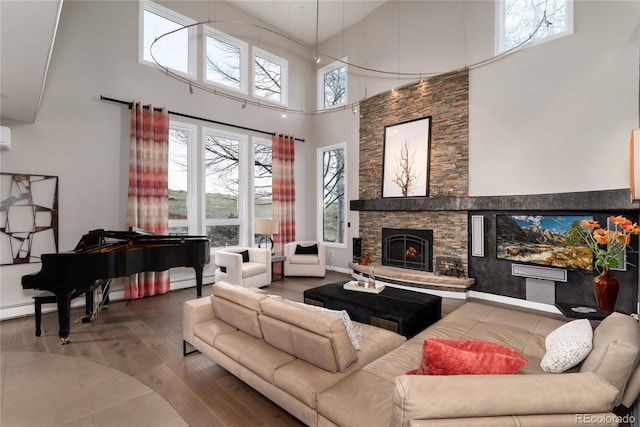 living area with a stone fireplace, baseboards, a towering ceiling, and wood finished floors