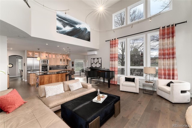 living room with an AC wall unit, dark wood finished floors, arched walkways, and a healthy amount of sunlight