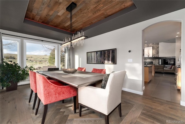 dining room with baseboard heating, baseboards, arched walkways, wooden ceiling, and wood finished floors