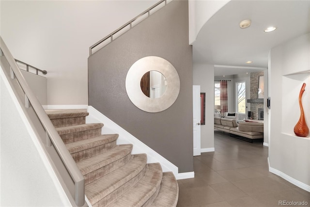 staircase featuring arched walkways, baseboards, a stone fireplace, and recessed lighting