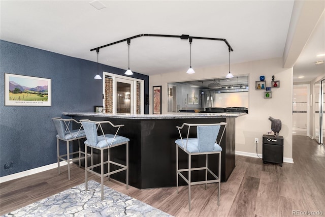 kitchen with a peninsula, wood finished floors, decorative light fixtures, a breakfast bar area, and baseboards