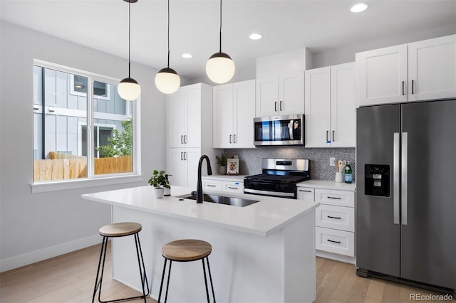kitchen with a sink, an island with sink, backsplash, white cabinets, and appliances with stainless steel finishes